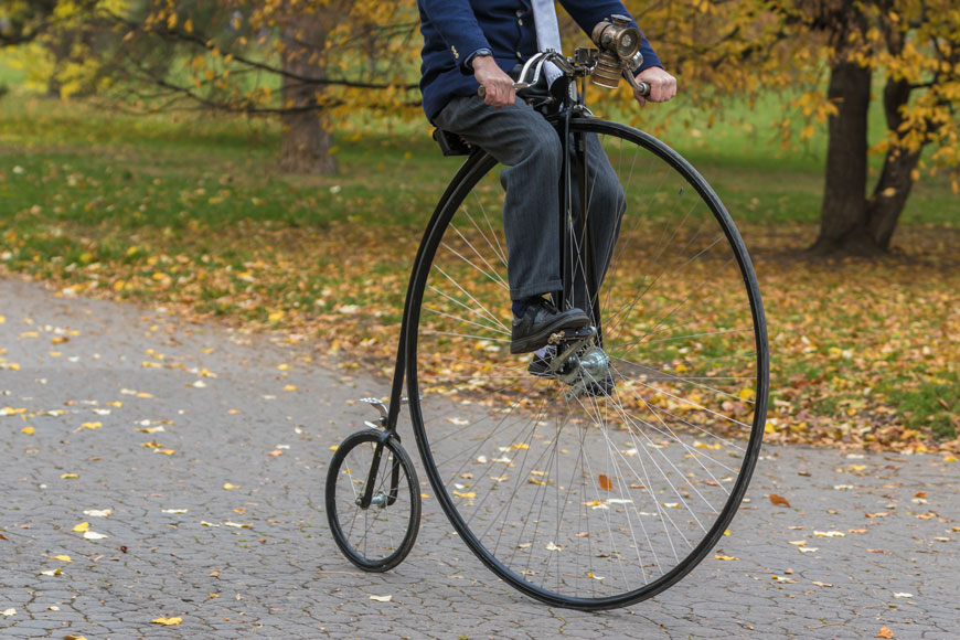 A man rides a penny farthing through a park in the autumn