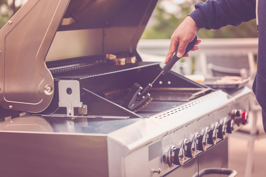 A man cleans a stainless steel grill with a brush