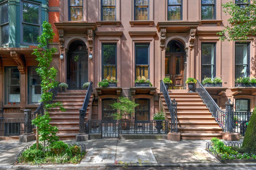 Traditional New York brownstones are framed by two small trees in tree pits on the sidewalk.