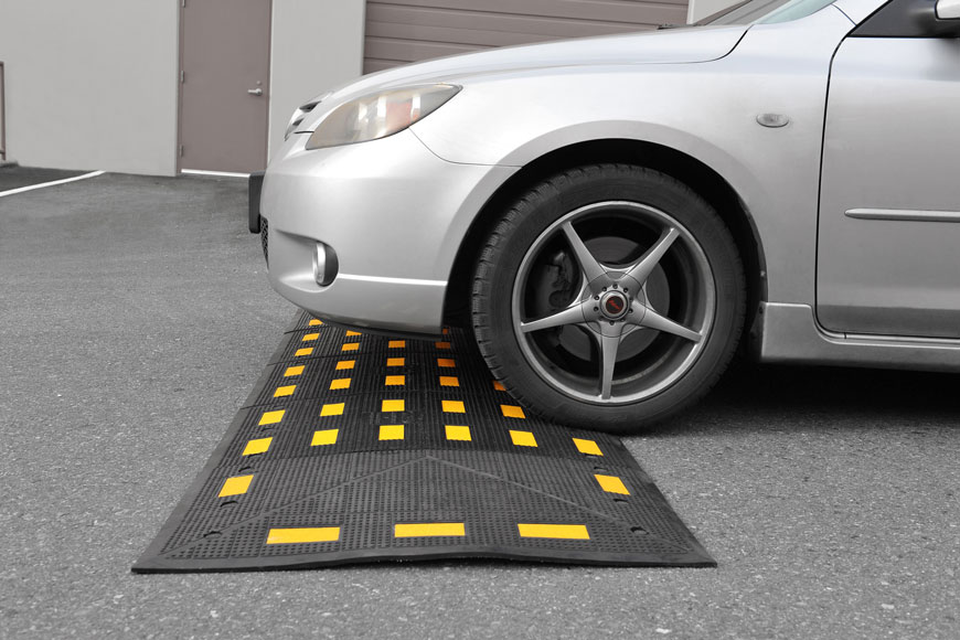 silver car sits on a rubber speed hump in a parking lot 