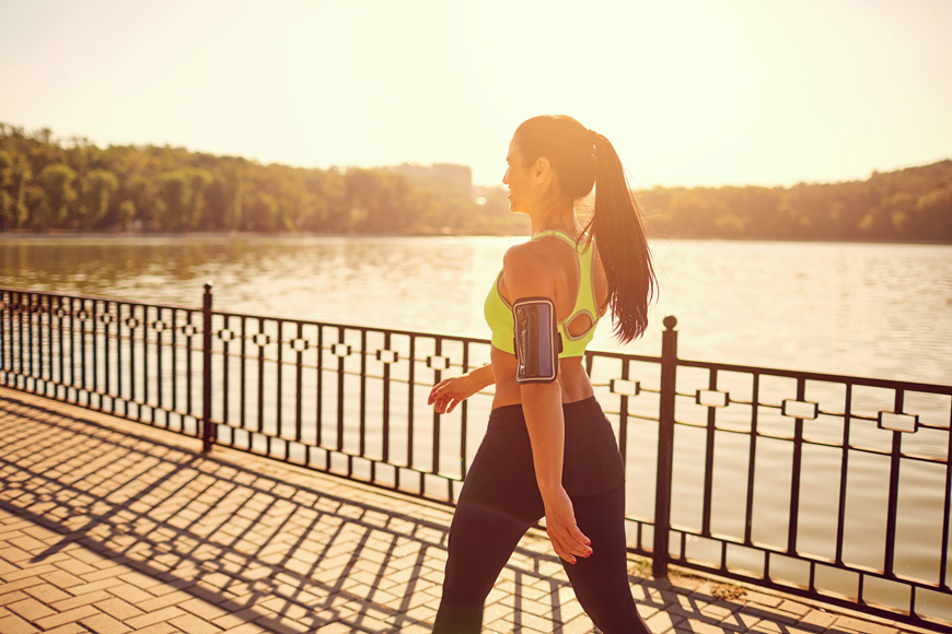 A woman gets exercise by walking along a paved path by the water