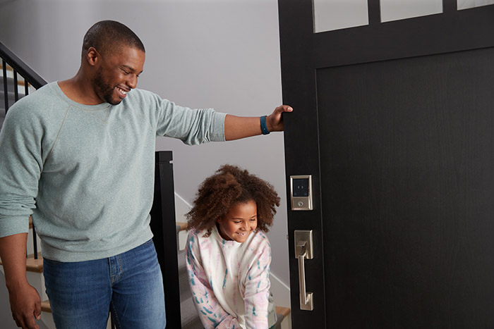 Dad holding front door open for daughter with Homekit smart lock on the door.